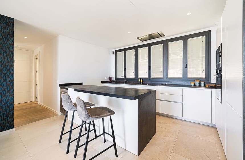 A minimalist kitchen featuring white handleless cabinetry, a dark grey island, and large dark-framed windows.