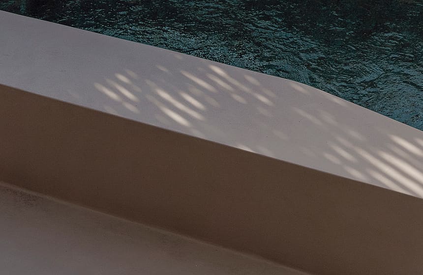 A close-up of a swimming pool edge featuring dark water and a smooth, neutral-toned concrete or stone coping.