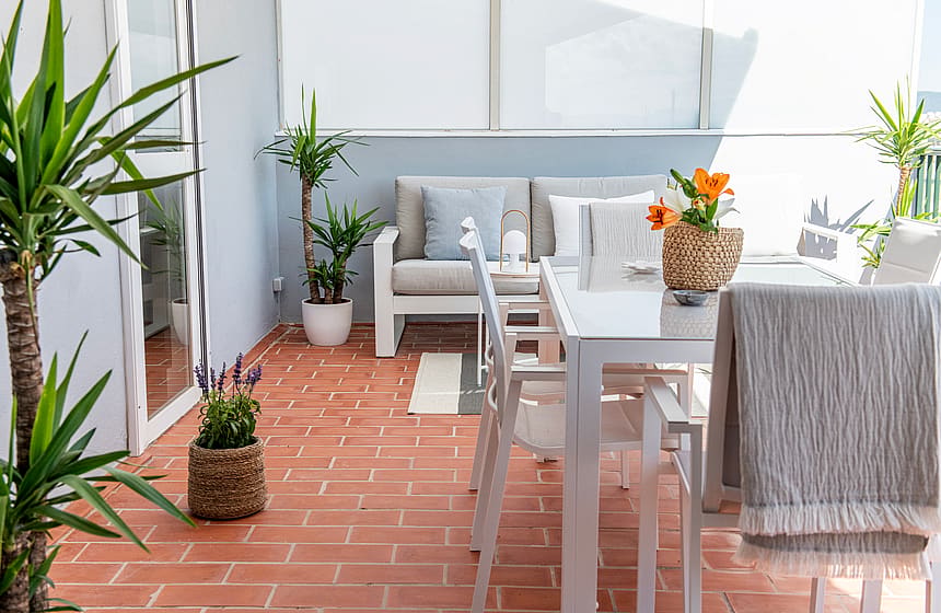 An outdoor terrace with terracotta tile flooring, a white dining table with matching chairs, and potted yucca plants.