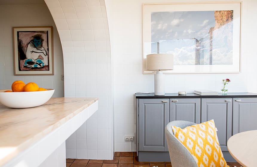 Interior view showing a white brick arch leading to a room, a grey sideboard with a table lamp, and a yellow patterned cushion.