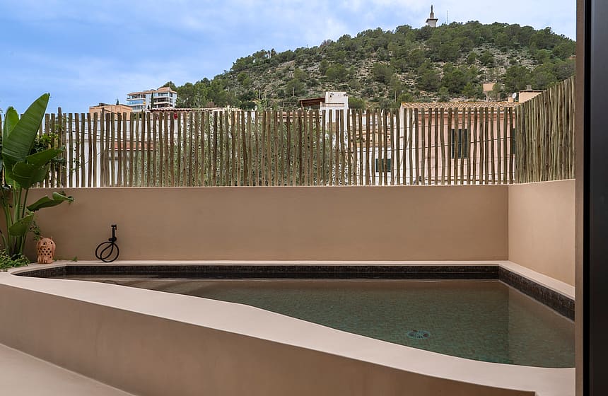 A small triangular plunge pool with beige rendered walls and a vertical bamboo privacy screen, set against a verdant hill.