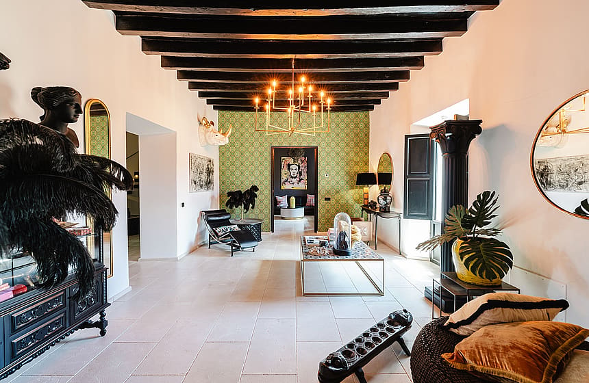 Spacious living room featuring dark exposed wooden ceiling beams, white walls, and decorative green wallpaper in a Sencelles property.