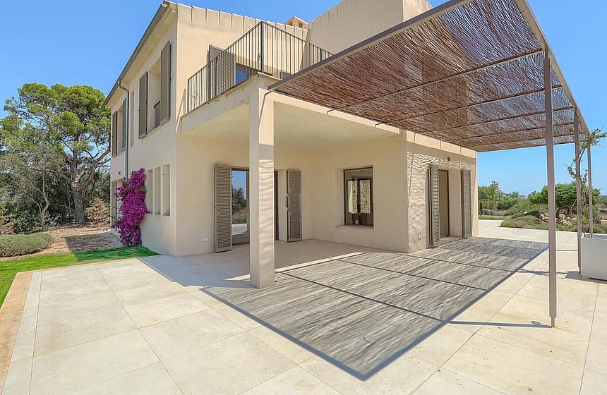 Exterior view of a beige stone finca in Santanyí featuring a large patio covered by a natural reed pergola.