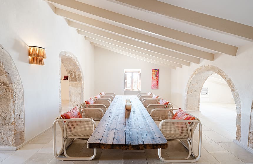 Dining room with a long wooden table, rattan chairs, and exposed stone arches under a pitched timber beam ceiling.