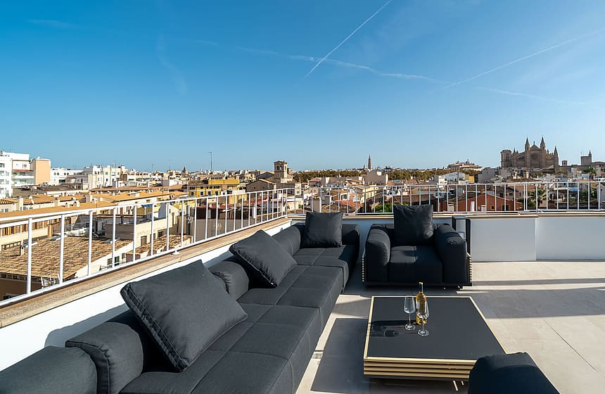 Modern black lounge furniture on a sun-drenched rooftop terrace overlooking Palma Old Town and the Cathedral.
