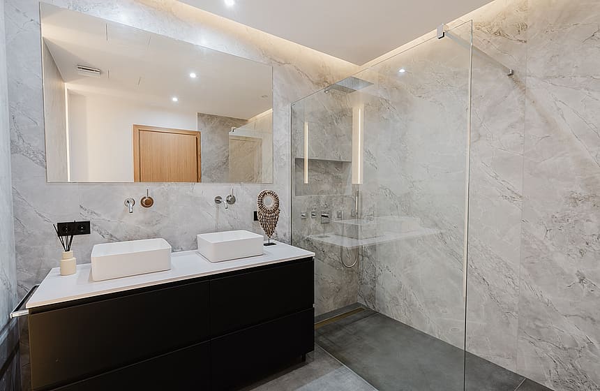 A modern bathroom featuring a dark vanity with two white vessel sinks, a wall-to-wall mirror, and a walk-in glass shower.