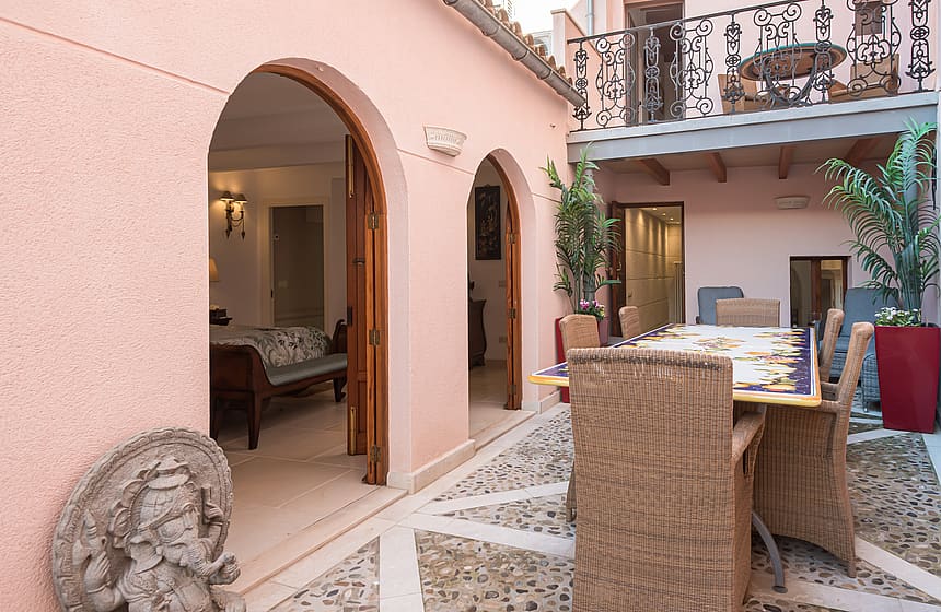 Pink-walled courtyard patio with a tiled dining table, potted plants and arched doorways