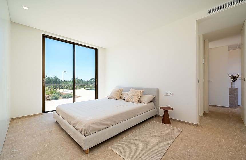 Minimalist bedroom with neutral linens, a natural fiber rug, and floor-to-ceiling sliding glass doors opening to a garden.