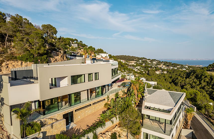 Aerial view of a contemporary multi-level villa with stone retaining walls and glass facade set into a hillside.