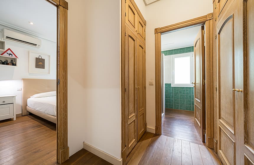 A corridor in a villa featuring natural wood built-in wardrobes and doorways leading into two bedrooms with wooden flooring.