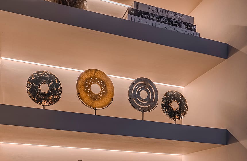 Floating shelves display ceramic art and decorative masks under integrated LED strips above a firewood storage area.