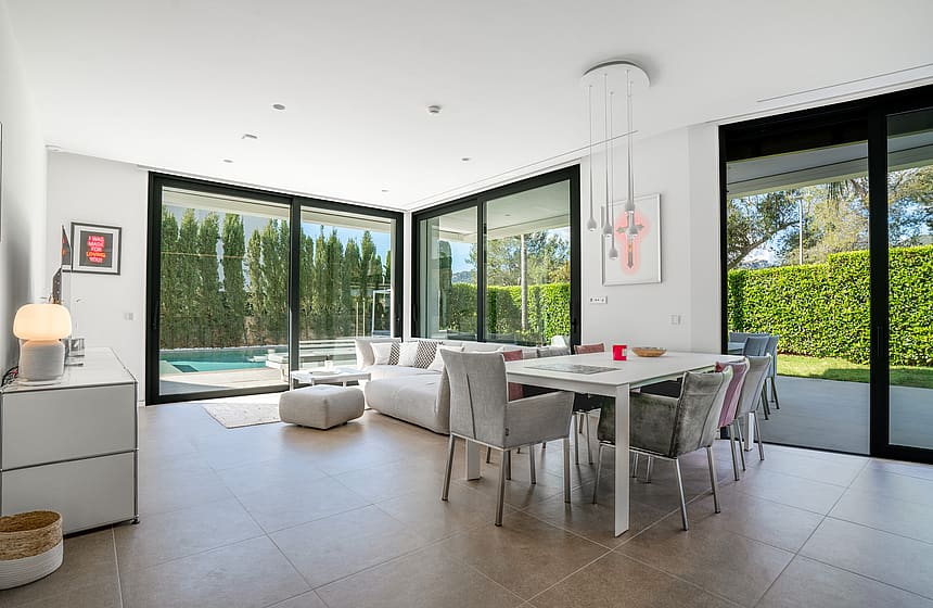 Open-plan living and dining room with corner sliding glass walls opening to the pool terrace and garden.