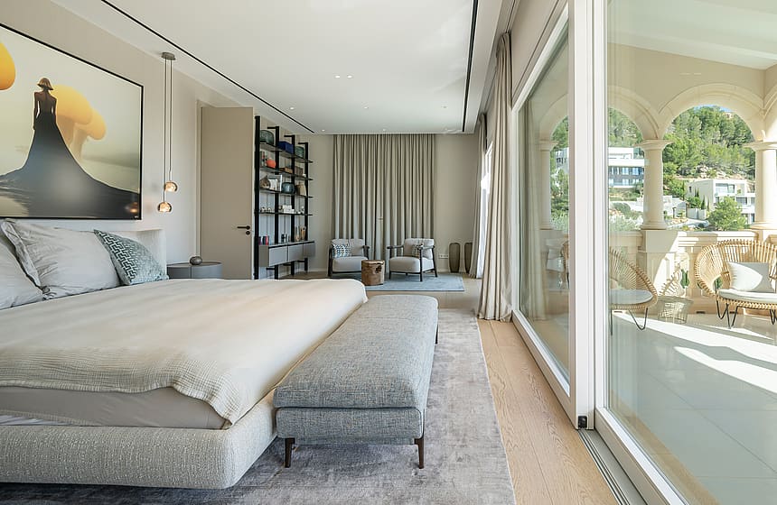 Master bedroom with a king-sized bed, soft grey fabrics, and open access to a private stone arched terrace in Son Vida.