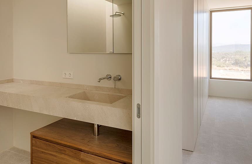 Contemporary bathroom featuring a floating wooden vanity, integrated stone sink, and a view through a sunlit hallway.