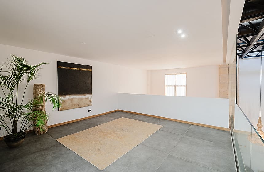 An open mezzanine landing with grey tiled flooring, white walls, and a large abstract painting, featuring a glass balustrade.