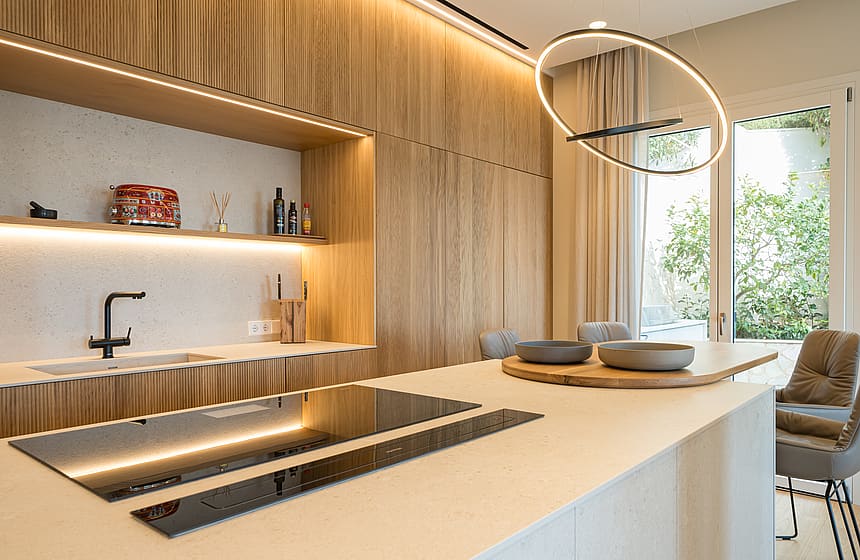 Modern kitchen featuring vertical oak slat cabinets, integrated lighting, a stone kitchen island, and a circular pendant light.