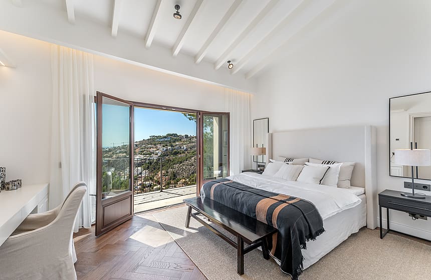 Bright bedroom with herringbone wood floors and open French doors leading to a terrace with sweeping valley views.