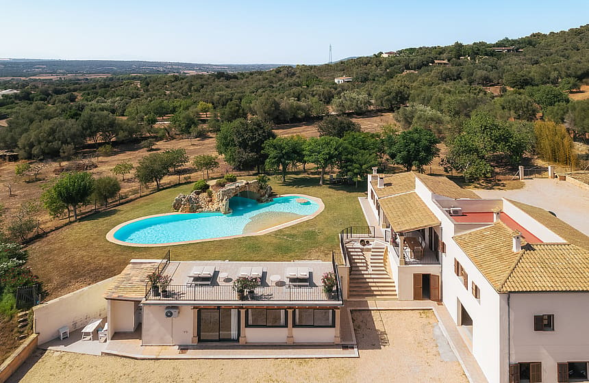 Vista aérea de finca en Manacor con piscina curva, tejados de teja y paisaje montañoso.