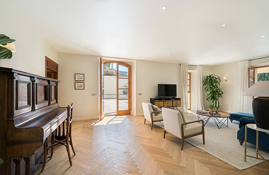 Bright living room featuring light oak herringbone parquet flooring, a classic upright piano, and arched patio doors.