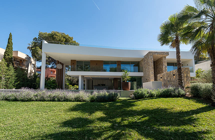 Exterior view of a modern two-story villa in Santa Ponsa, featuring stone walls, glass balconies, and a manicured garden.