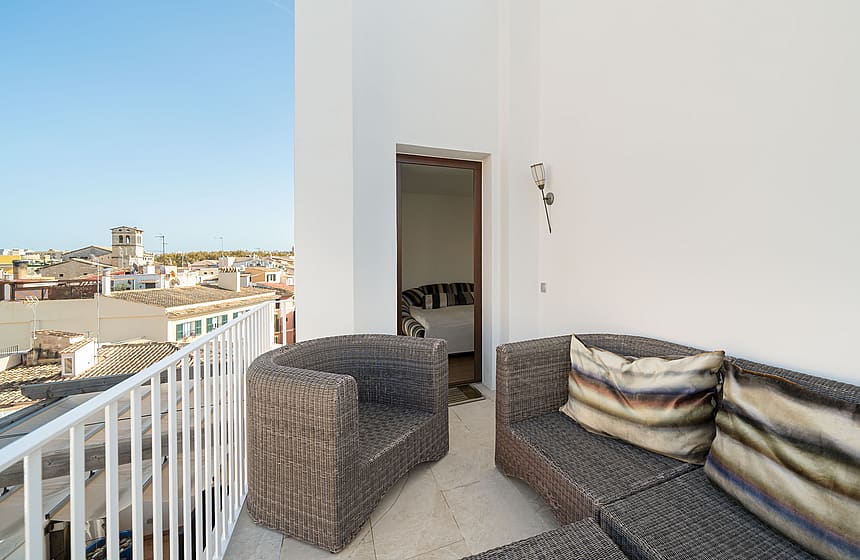 Rooftop terrace with grey wicker lounge furniture and white railings overlooking the historic city of Palma.