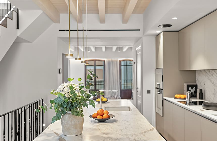 A white marble kitchen island featuring brass pendant lights, floral arrangements, and exposed light wood ceiling beams.