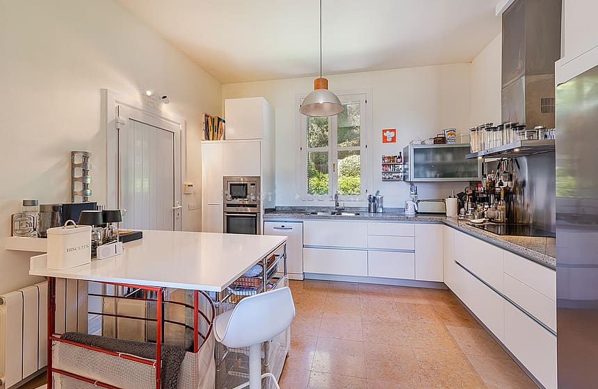 Contemporary white kitchen with stainless-steel appliances, island workstation, and glass doors opening to terrace