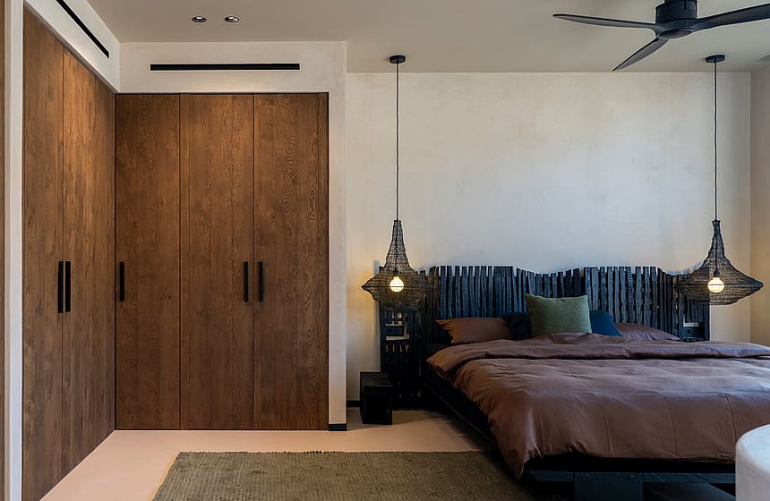 A modern bedroom featuring dark wood built-in wardrobes, a bed with a charred timber headboard, and pendant lights.