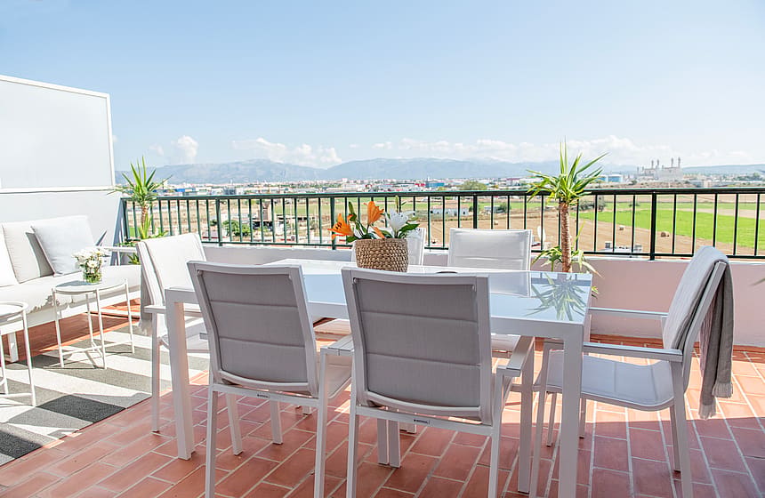 Rooftop terrace in El Molinar featuring a white dining set and outdoor sofa overlooking distant mountains under a clear sky.