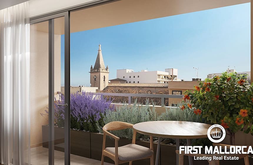 A modern apartment terrace featuring a small wooden table and chair, looking out over the Santa Catalina cityscape under a clear blue sky.
