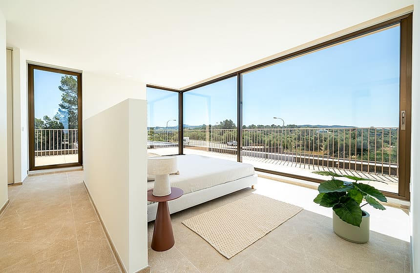A modern master bedroom with minimalist decor, white bed, stone flooring, and expansive glass walls looking out over green hills.