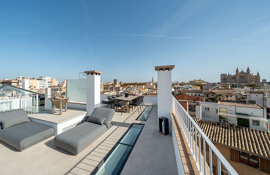 Large rooftop terrace with grey loungers, glass skylights, and panoramic views of Palma Old Town and the Cathedral.