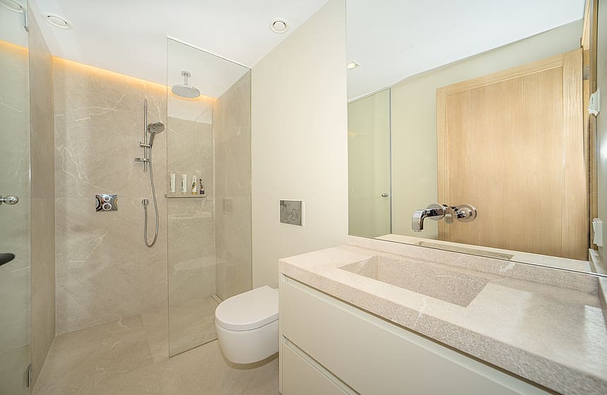 Modern bathroom featuring a beige stone tiled walk-in shower with glass partition, white vanity, and large mirror.