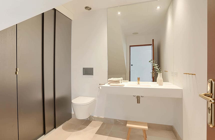 A minimalist bathroom featuring a wall-hung white basin, a wall-mounted toilet, and tall grey floor-to-ceiling cabinetry.