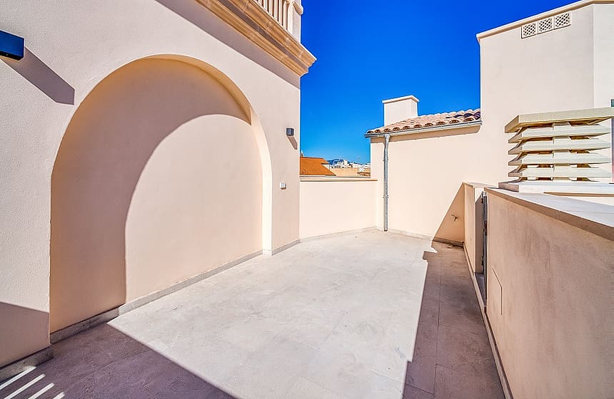 Empty rooftop terrace in Old Town with beige stucco walls, a large arched niche, and views toward traditional tiled rooftops.