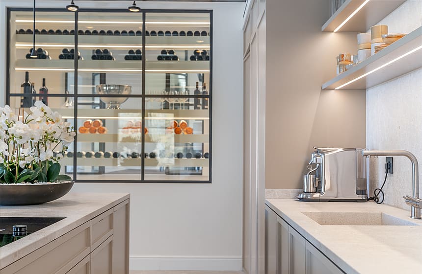 View from a kitchen island toward a temperature-controlled wine storage area with glass and black metal framing.