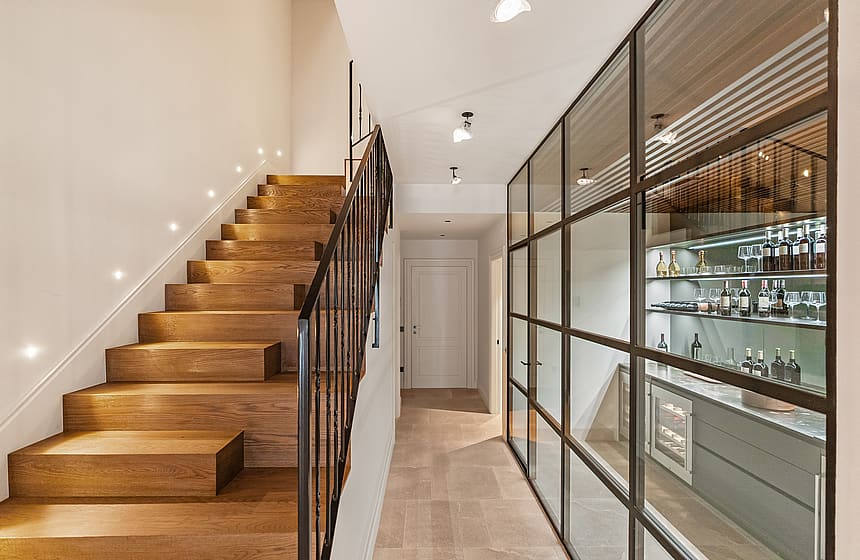 Contemporary hallway featuring a black steel-framed glass wine cellar next to a wooden staircase with iron railings.