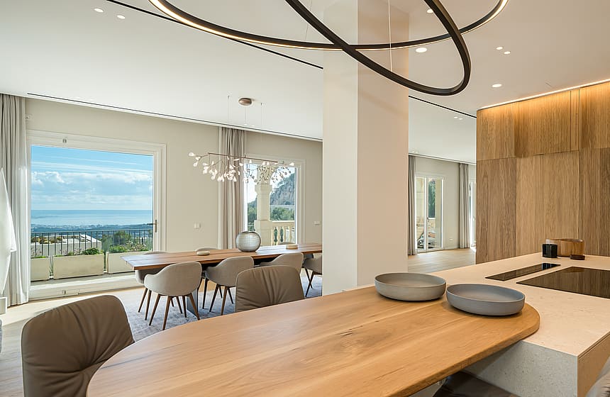 Open plan kitchen with light wood breakfast bar and modern dining set overlooking the Mediterranean coastline.