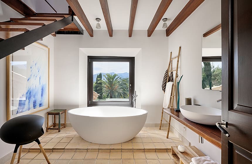 A modern bathroom with a freestanding white soaking tub on a tiled platform, centered before a window with mountain views.