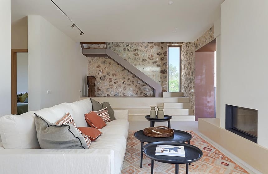 Interior view of a living room featuring a cream sofa, stone accent wall, inset fireplace, and floating staircase steps.