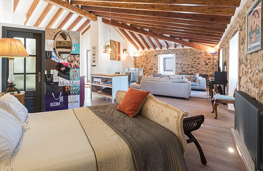 Loft-style bedroom featuring exposed wooden beams, stone walls, and an integrated living space.