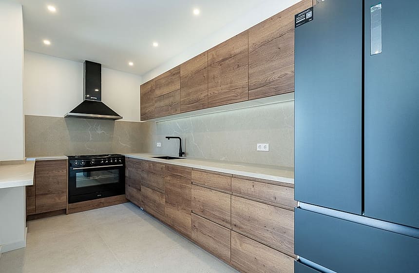 A modern kitchen in a townhouse featuring wood grain cabinets, dark appliances, stone countertops, and recessed ceiling lights.