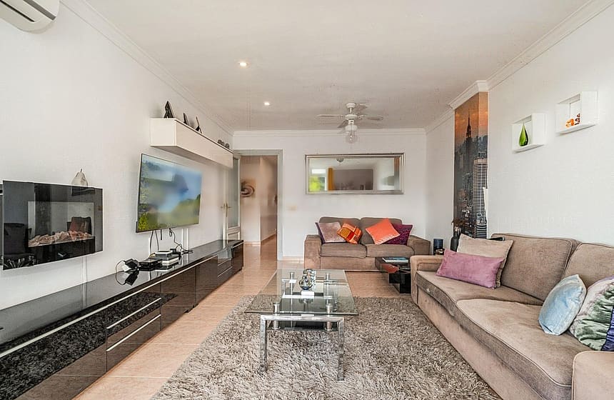 Living room featuring a brown sofa, glass coffee table, wall-mounted electric fireplace, and dark glossy media console.