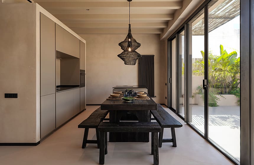 Modern kitchen with minimalist grey cabinetry and a dark wood dining table, opening onto a sunlit outdoor terrace.