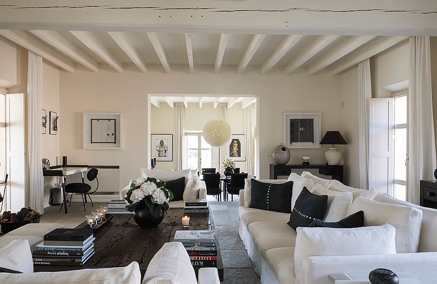 Spacious living room with white sofas, dark wooden coffee table, and beamed ceilings in a finca setting.