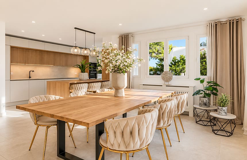Renovated open-plan kitchen with oak cabinetry, dining table with cream tufted chairs and pendant lights