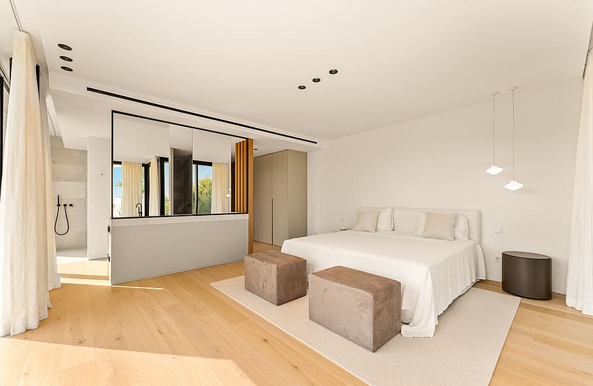 Contemporary bedroom with light oak flooring, white walls, and a central partition wall with a mirror and glass window.