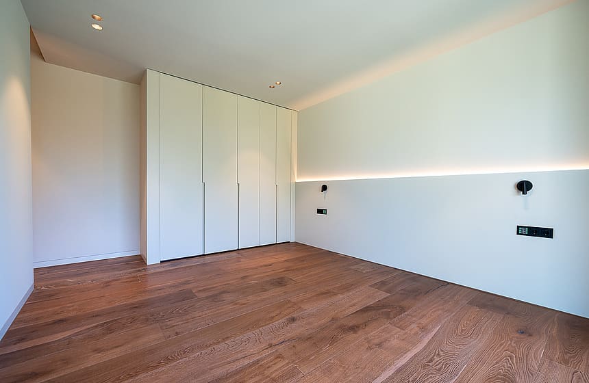 A minimalist bedroom featuring light-toned walls, oak wood flooring, and built-in floor-to-ceiling closets.