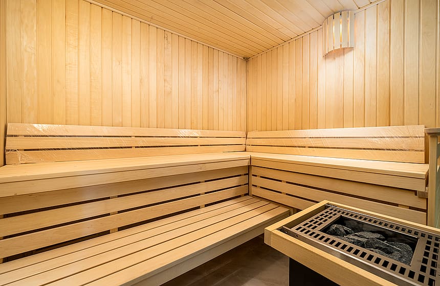 A modern home sauna featuring natural light wood wall cladding and tiered wooden bench seating, with a central electric heater.