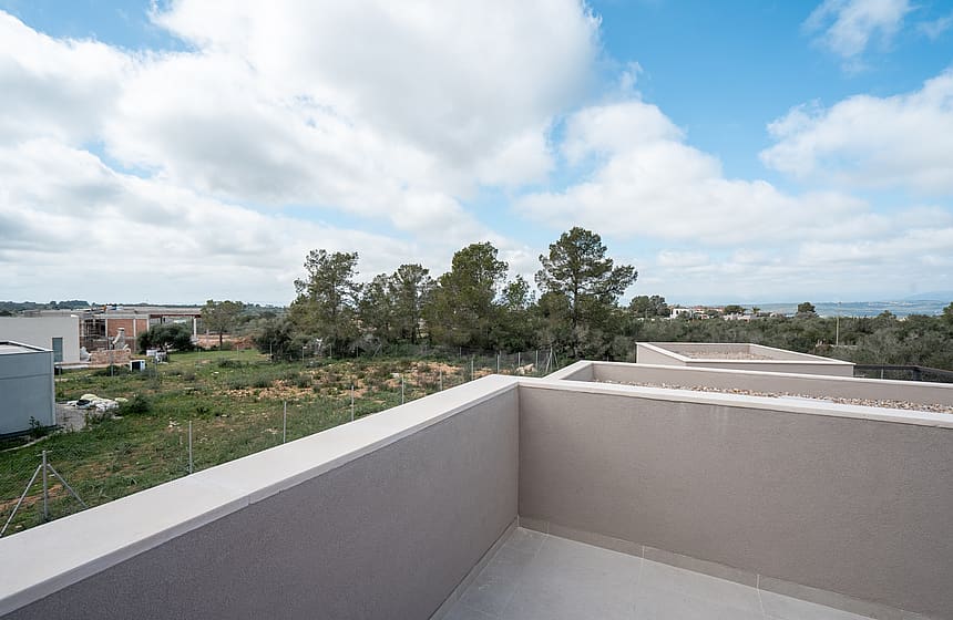 A wide angle view from a minimalist terrace with stone parapets overlooking a landscaped garden and distant mountains.